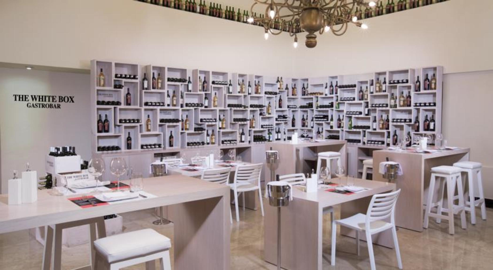 Grand Oasis Palm Hotel Cancún Kültér fotó The photo shows a modern restaurant interior. The walls are lined with shelves that display a variety of bottles, likely wine or spirits, creating a visually striking backdrop. The dining area features wooden tables and white chairs, offering a clean