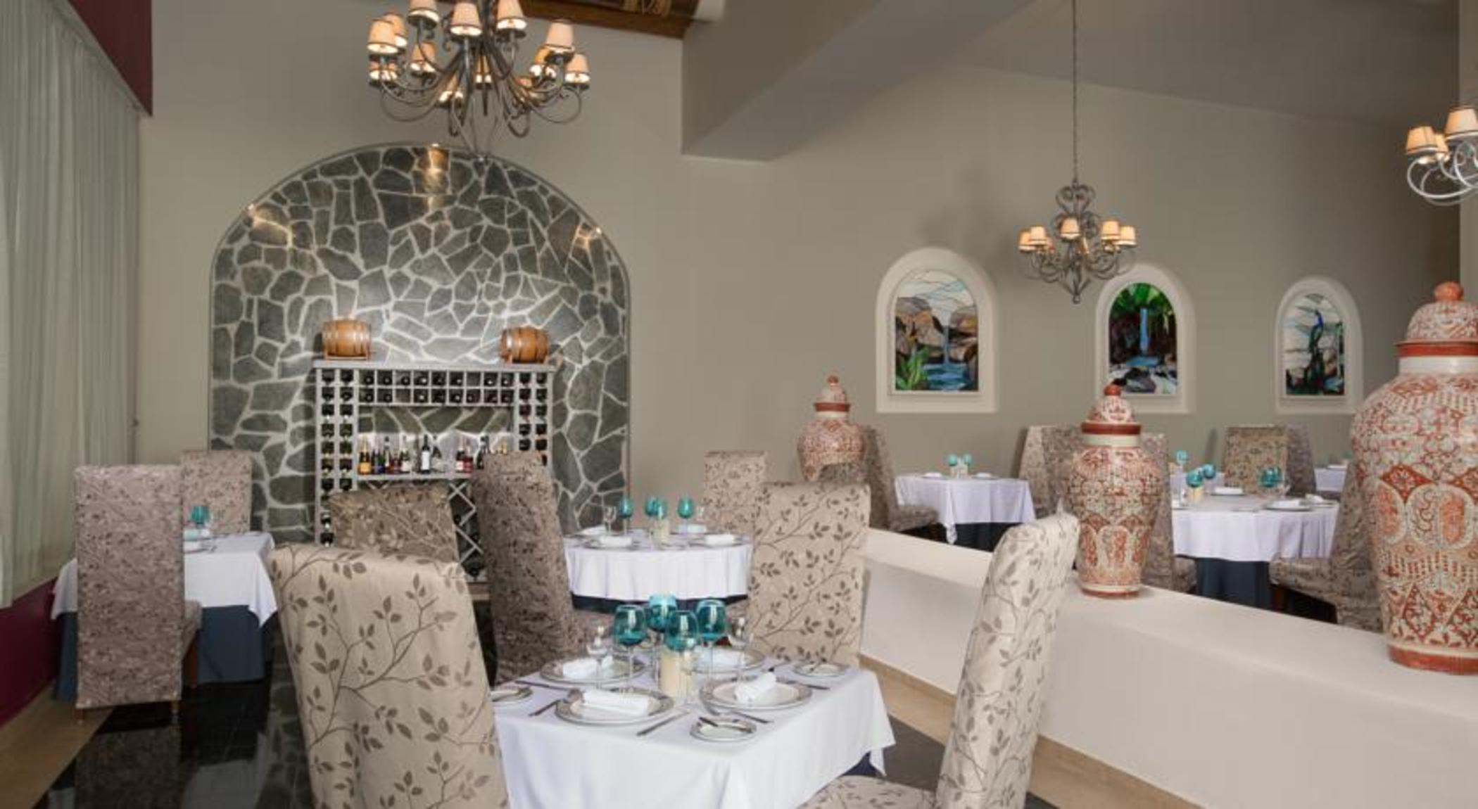 Grand Oasis Palm Hotel Cancún Kültér fotó The photo shows an elegant restaurant interior. There are several tables set with white tablecloths and neatly arranged diningware, including glasses. The seating features plush chairs that have a floral design. 

In the background, there is a decora