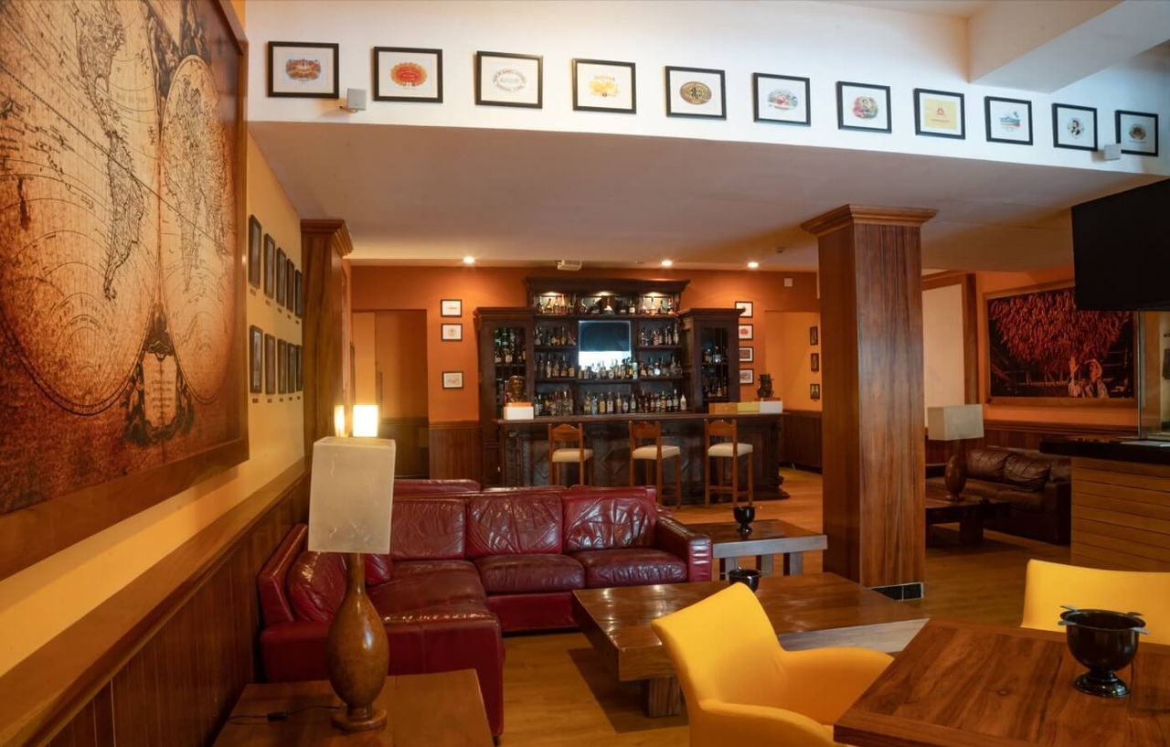 Grand Oasis Palm Hotel Cancún Kültér fotó The photo shows a cozy interior of a bar or lounge area. It features a comfortable setup with a deep red leather sofa and wooden tables. The walls are adorned with decorative artwork, including various framed pictures that add character to the space.